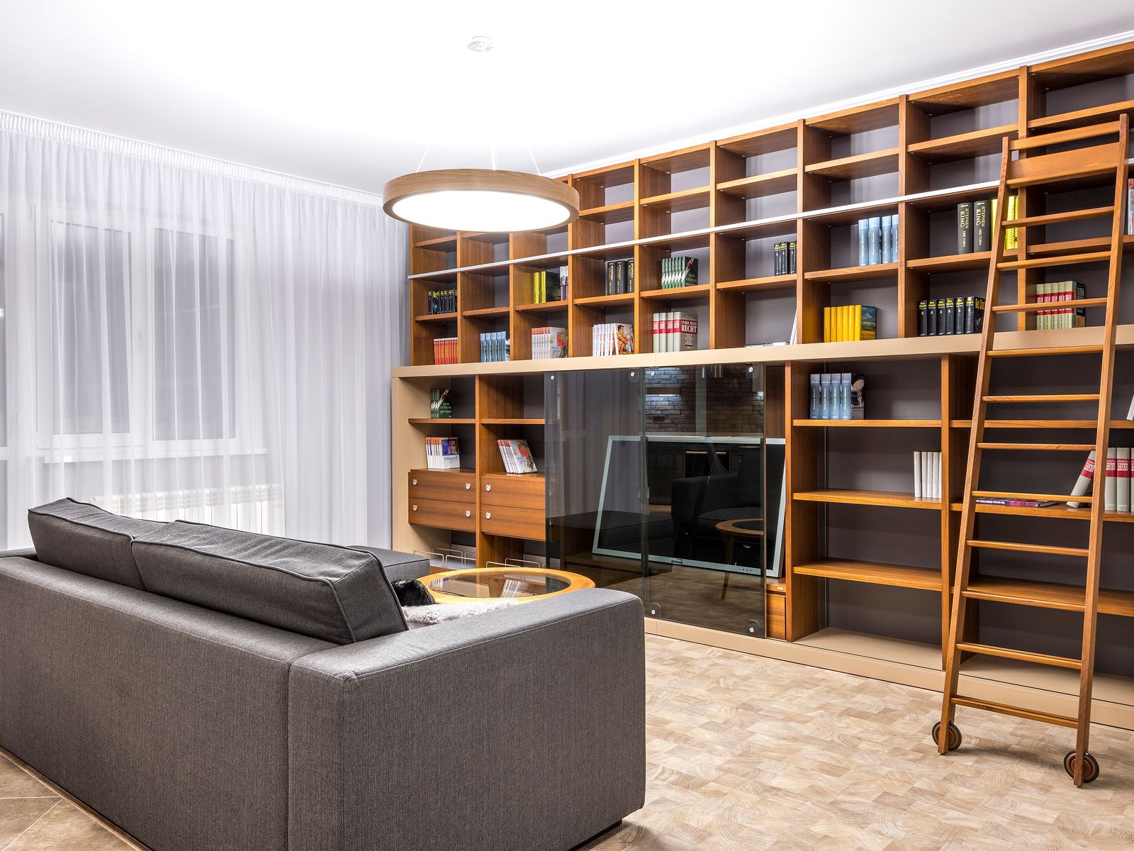 Bibliothèque en bois montée du sol au plafond, le long d’un mur de séjour, avec une échelle de bibliothèque à roulettes accrochée à son rail.