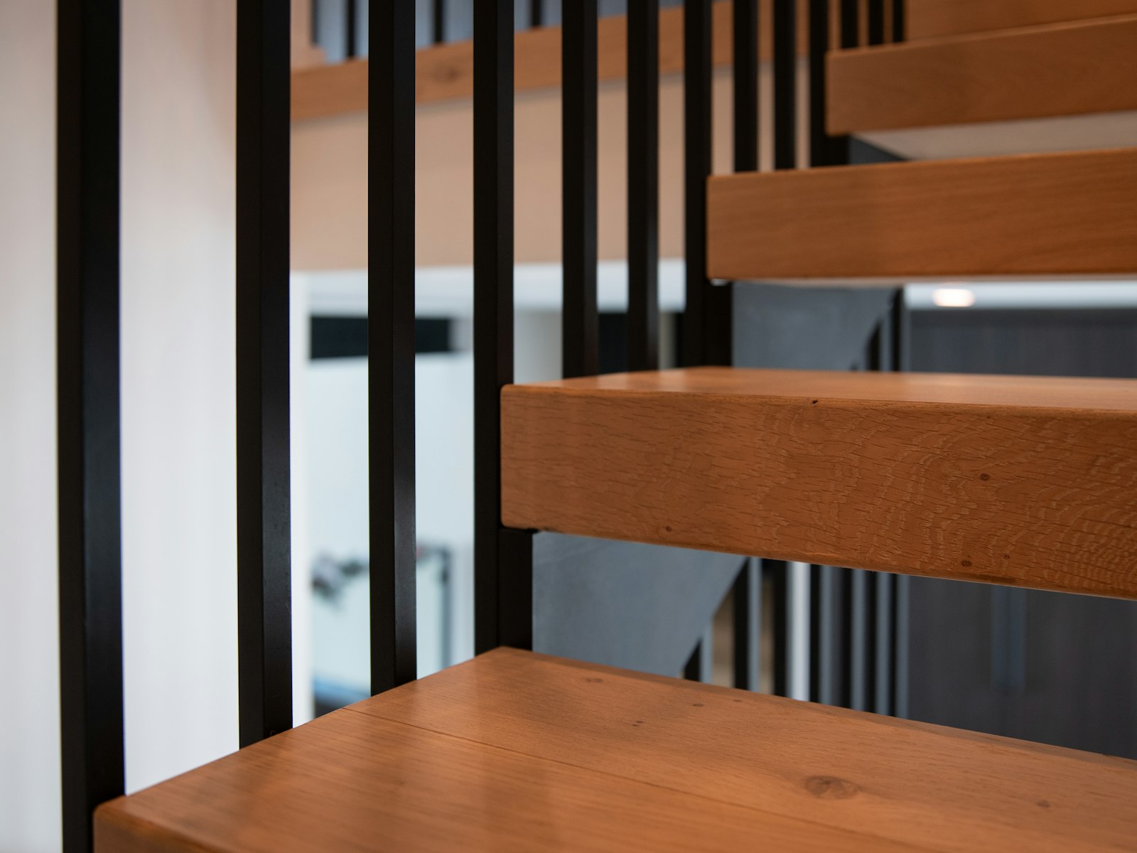 Escalier à marches suspendues en chêne clair, encastrées dans un limon métallique noir.