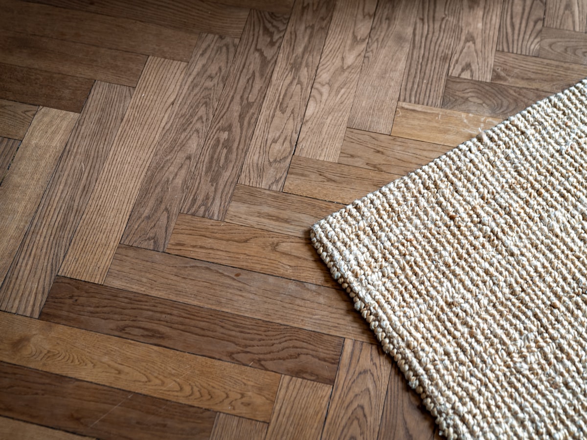 Parquet en chêne posé en bâtons rompus, avec le coin d’un tapis en jute tressé posé dessus.
